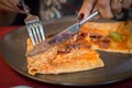 Woman hand cutting of a portion of delicious crepe with meat served on a grey plate.