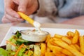 Woman hand dipping delicious French fries into mayonnaise sauce, cheese sauce.