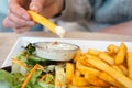 Woman hand dipping delicious French fries into mayonnaise sauce, cheese sauce.