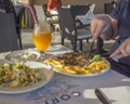 Woman hand eating Greek meal in greek tavern on corfu, grilled pork steak with french fries and farmers salad, tzatziki