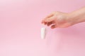 Woman hand folding white tampon on pink background, copy space