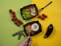 Woman hand with a fork reaching for food in takeaway box: rice with fish in sauce, chicken with buckwheat, vegetables and greens Royalty Free Stock Photo