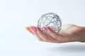 Woman hand with gel polish shellac manicure holds a trendy New Year or Christmas decoration - a shiny wire ball on a white Royalty Free Stock Photo