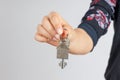 Woman hand giving a new metal key with home shaped keychain, isolated. New home concept