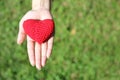 Woman hand giving red hand-made crocheted heart with green grass background and copy space. Valentine Day. Symbol of love. Royalty Free Stock Photo