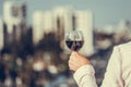 Woman hand with glass of red wine against the city background at summer evening. Royalty Free Stock Photo