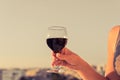 Woman hand with glass of red wine against the city background at summer evening. Royalty Free Stock Photo