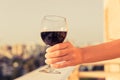 Woman hand with glass of red wine against the city background at summer evening. Royalty Free Stock Photo