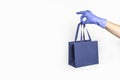 Woman hand in glove with gift paper bag on white background. Delivery of food, groceries, home shopping. Protection for COVID-19