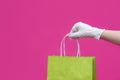 Woman hand in glove with paper bag on pink background. Delivery of food, groceries, home shopping. Protection for COVID-19