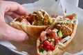 Woman hand hold an authentic fresh falafels balls inside of half pita bread sandwich with chopped salad and drizzle of tahini