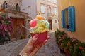 Woman hand hold sweet ice - cream cone with different flavors held in hand on the background of old street in Porec