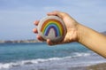 Woman hand hold pebble with painted rainbow against sea