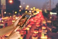 Woman hand hold and touch screen smart phone over blurred photo of car on the road with bokeh background of city street night ligh Royalty Free Stock Photo