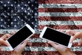 Woman hand hold and touch screen on smartphone or cellphone over blurred America flag on clacked wall background.