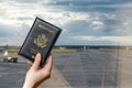 Woman hand holding american passport in the airport waiting zone looking through the window at planes.