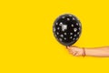 Woman hand holding a black balloon with white puppy paws on a yellow background