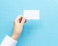 Woman hand holding blank business name card paper isolated on blue background with copy space.