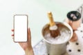 Woman hand holding blank white screen mobile phone with champagne bottle in ice bucket and two glasses near jacuzzi pool Royalty Free Stock Photo