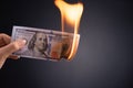 Woman hand holding burning burning dollar cash money over black background - business finances, savings and bankruptcy concept