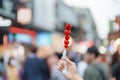 woman hand holding caramel coated strawberry skewer at night market. Street Food and travel concept