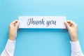 Woman hand holding card with the word thank you on blue background, studio shot.