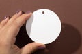 Woman hand holding cardboard white blank tag of round shape with little hole for clothes in upper part in center of