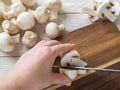 Woman hand holding a champignon halved with sharp knife on a wooden cutting board. Mushrooms as vegetable protein, raw food diet,