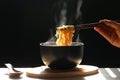 Woman hand holding chopsticks of instant noodles in cup with smoke rising dark background, Sodium diet high risk kidney failure,