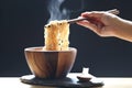 Woman hand holding chopsticks of instant noodles in cup with smoke rising and garlic on dark background, Sodium diet high risk