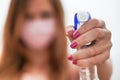 Woman hand holding cleaning disinfect or cleaning spray pointing to camera, blurred face with pink virus mask in background. Royalty Free Stock Photo