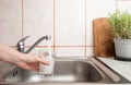 Woman hand holding a clear glass under a stream of fresh tap water from a kitchen sink faucet , soft focus close up Royalty Free Stock Photo