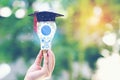 Woman hand holding cog inside in light bulb with graduates hat on natural green background, Education and Creative idea and Royalty Free Stock Photo