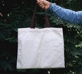 woman of hand holding cotton Tote Bag on green leaf background.