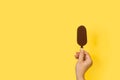 Woman hand holding a dark chocolate dipped ice lolly on a yellow background