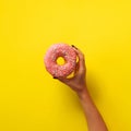 Woman hand holding delicious pink donut on yellow color background. Top view banner with copy space. Sweet, dessert, diet concept Royalty Free Stock Photo