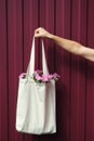 Woman hand holding eco reusable blank canvas shopping bag with flowers inside on red background. Zero waste mock-up. Vertical Royalty Free Stock Photo