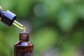 Woman hand holding essential oil or vitamin C dropping to the bottle on natural green background, Cosmetic pipette and spa concept