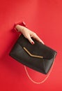 Woman hand holding fashion handbag through the hole in red paper background. Chic, style, fashion collection, trends, beauty blog Royalty Free Stock Photo