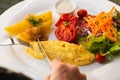 Woman hand holding fork and knife eating breakfast with omelet potato, tomatoes and vegetable salad on table. Royalty Free Stock Photo