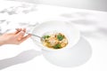 Woman hand holding fork with sea scallop over creamy risotto. Person eat seafood risotto with scallops. Female hand with italian