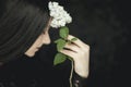 Woman hand holding fresh white lilac flowers to her face, very dark atmospheric sensual rural studio shot
