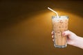 Woman hand holding the glass iced coffee on brown grungy wall