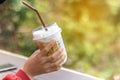 Woman hand holding the glass iced coffee on green nature background.
