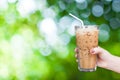 Woman hand holding the glass iced coffee on green nature background