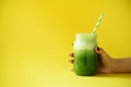 Woman hand holding glass jar of green smoothie, fresh juice against yellow background. Healthy beverage, vegan, vegetarian concept Royalty Free Stock Photo