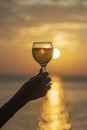 Woman hand holding glass of wine against a beautiful sunset near sea on the tropical beach, close up Royalty Free Stock Photo