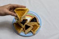 Woman hand holding hamantash cookie on top of colorful plate with more hamantash cookies