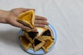 Woman hand holding hamantash cookie on top of colorful plate with more hamantash cookies