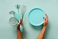 Woman hand holding kitchen utensils on pastel blue background. Baking tools - plate, brush, whisk, spatula. Bakery, cooking, Royalty Free Stock Photo